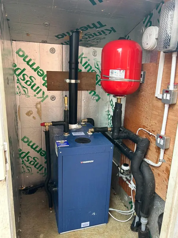 Blue Warmflow boiler in an insulated boiler house, with a red expansion vessel and lagged pipework