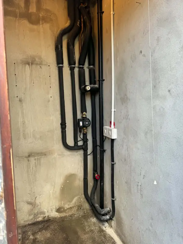 Black insulated heating pipework and a pump fixed to a wall
