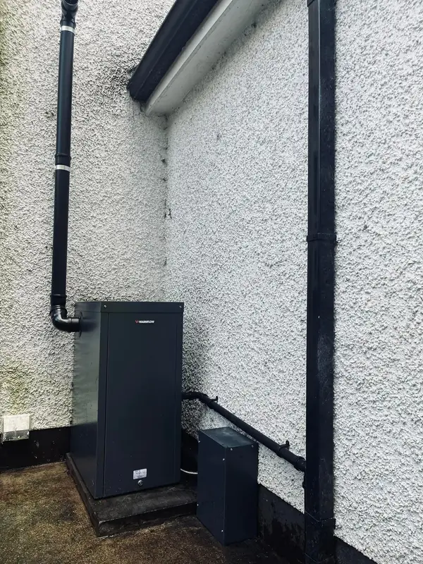 External oil boiler fitted in the corner of a pebble-dashed house, black flue pipe running up the wall