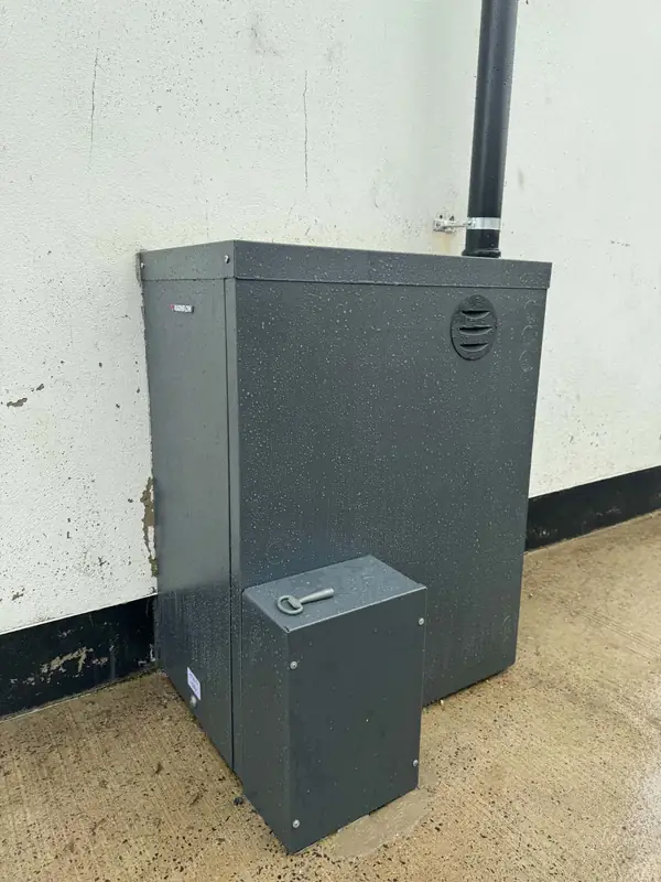 Outdoor Warmflow oil boiler against a white wall, black flue pipe running up the wall