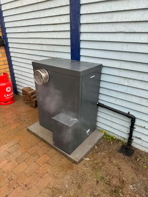 Outdoor Warmflow oil boiler on a concrete base, steam rising from the flue